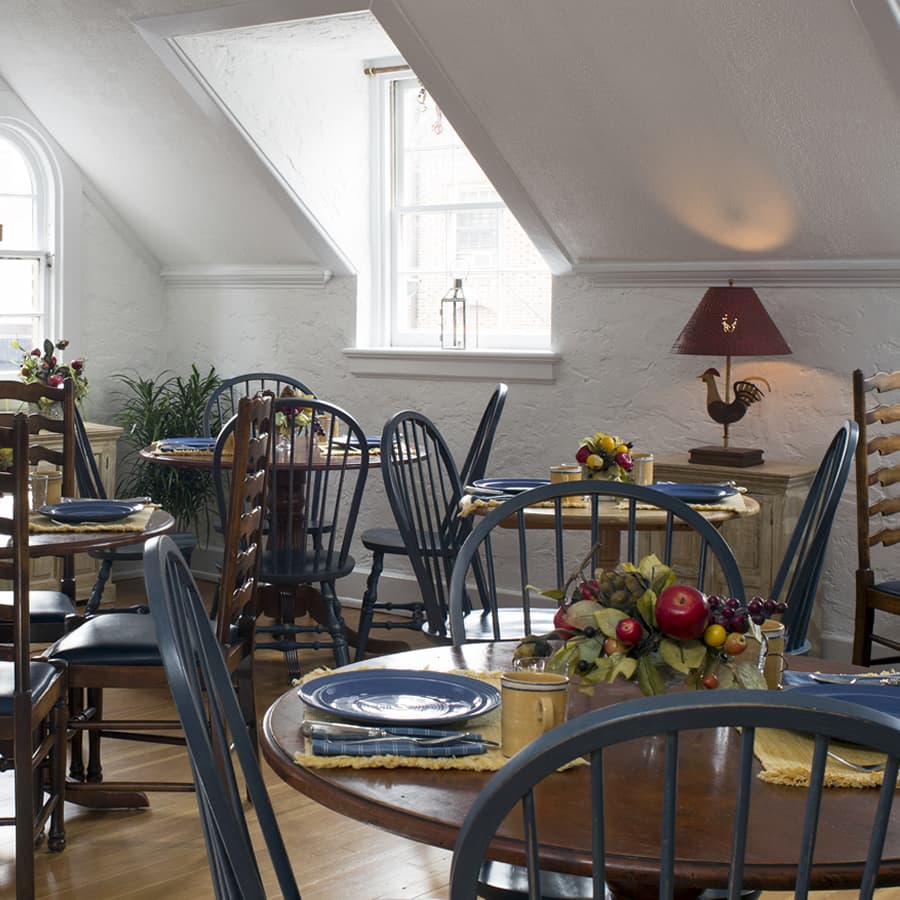 A dining room with several wood round tables set with blue plates and yellow coffee mugs.