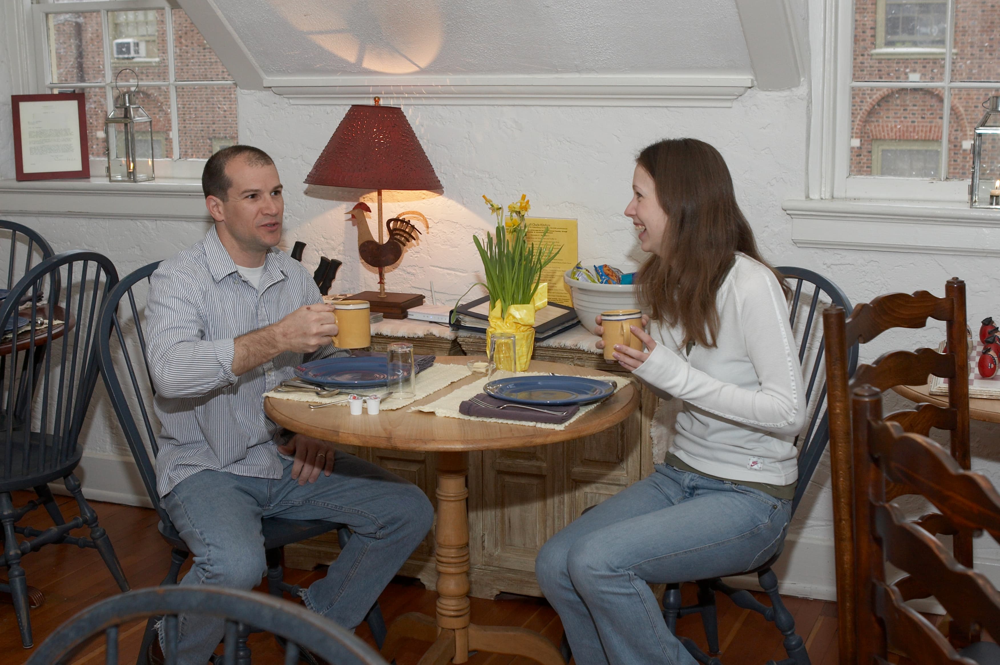 Man and woman sitting at round pine breakfast table drinking coffee out of yellow mugs