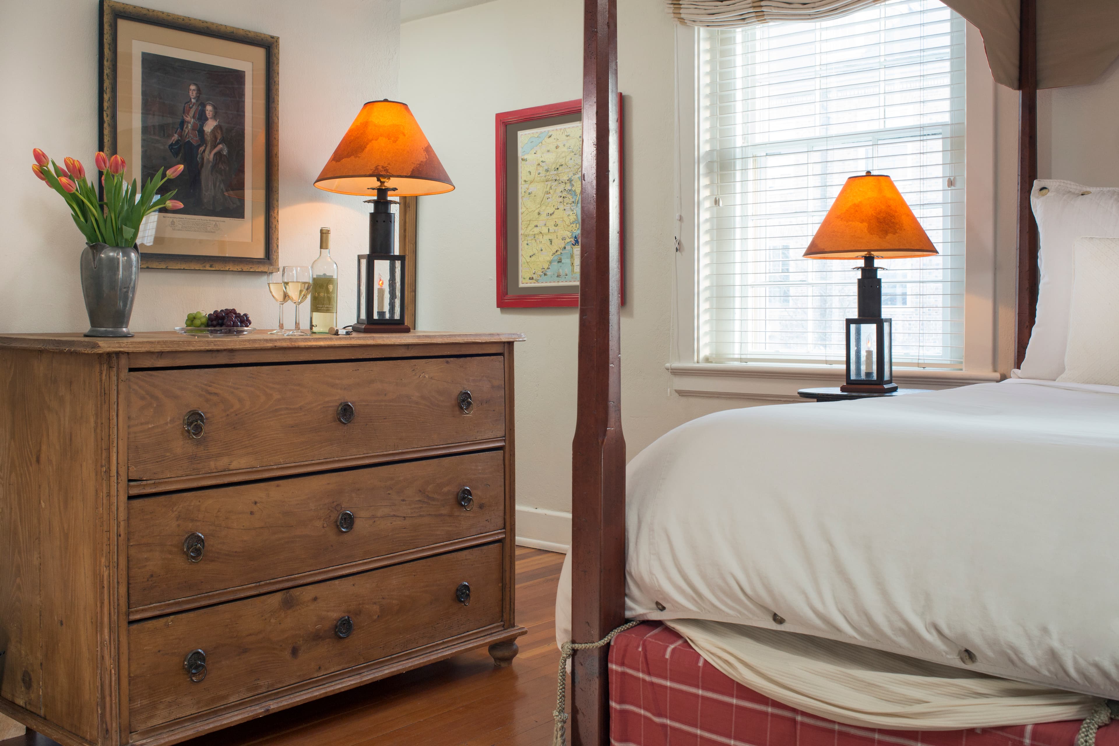 Partial view of four-poster canopy bed, large chest of drawers, table lamps, and vase with tulips