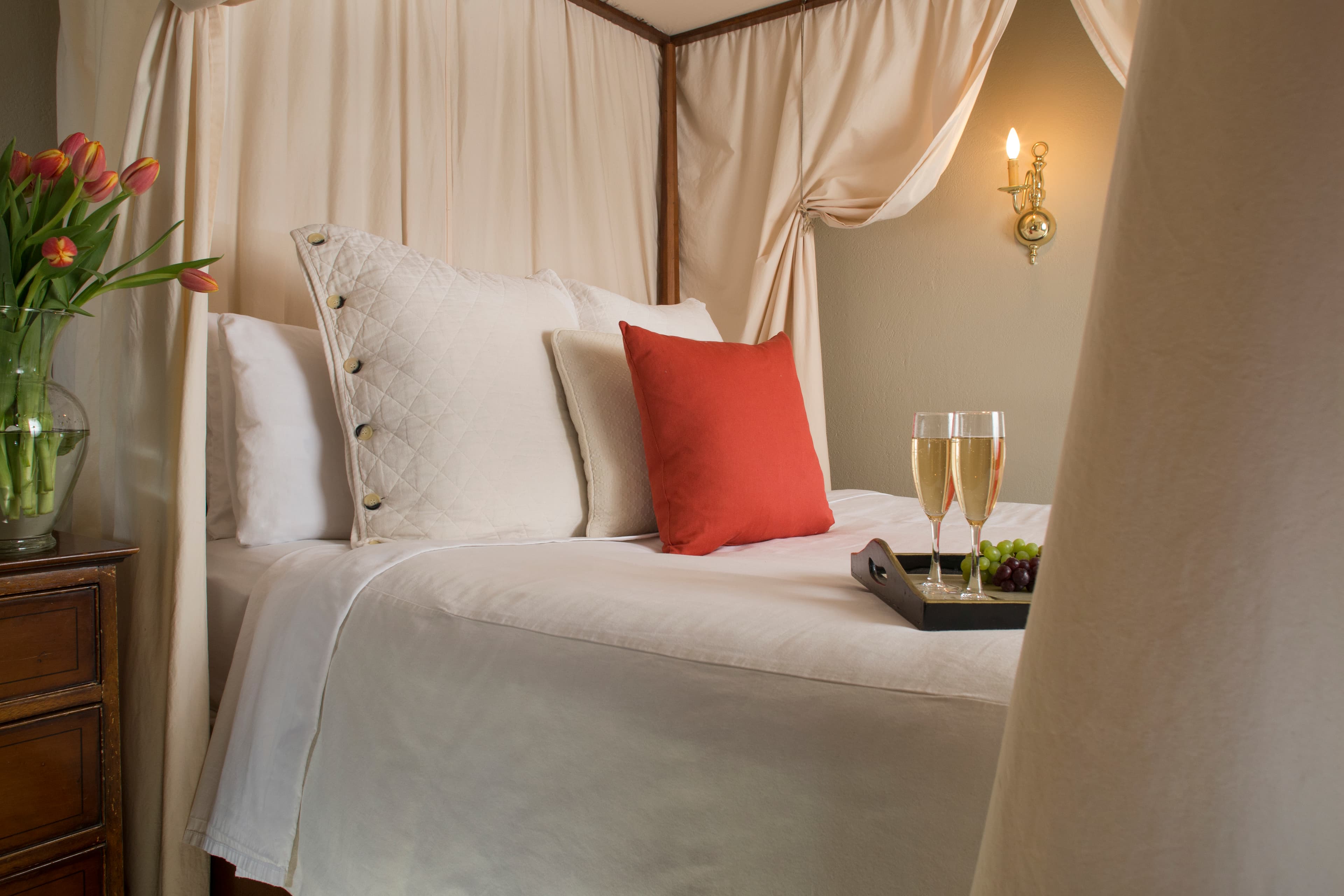 Close up of canopied four-poster bed with decorative pillows and tray with two champagne flutes