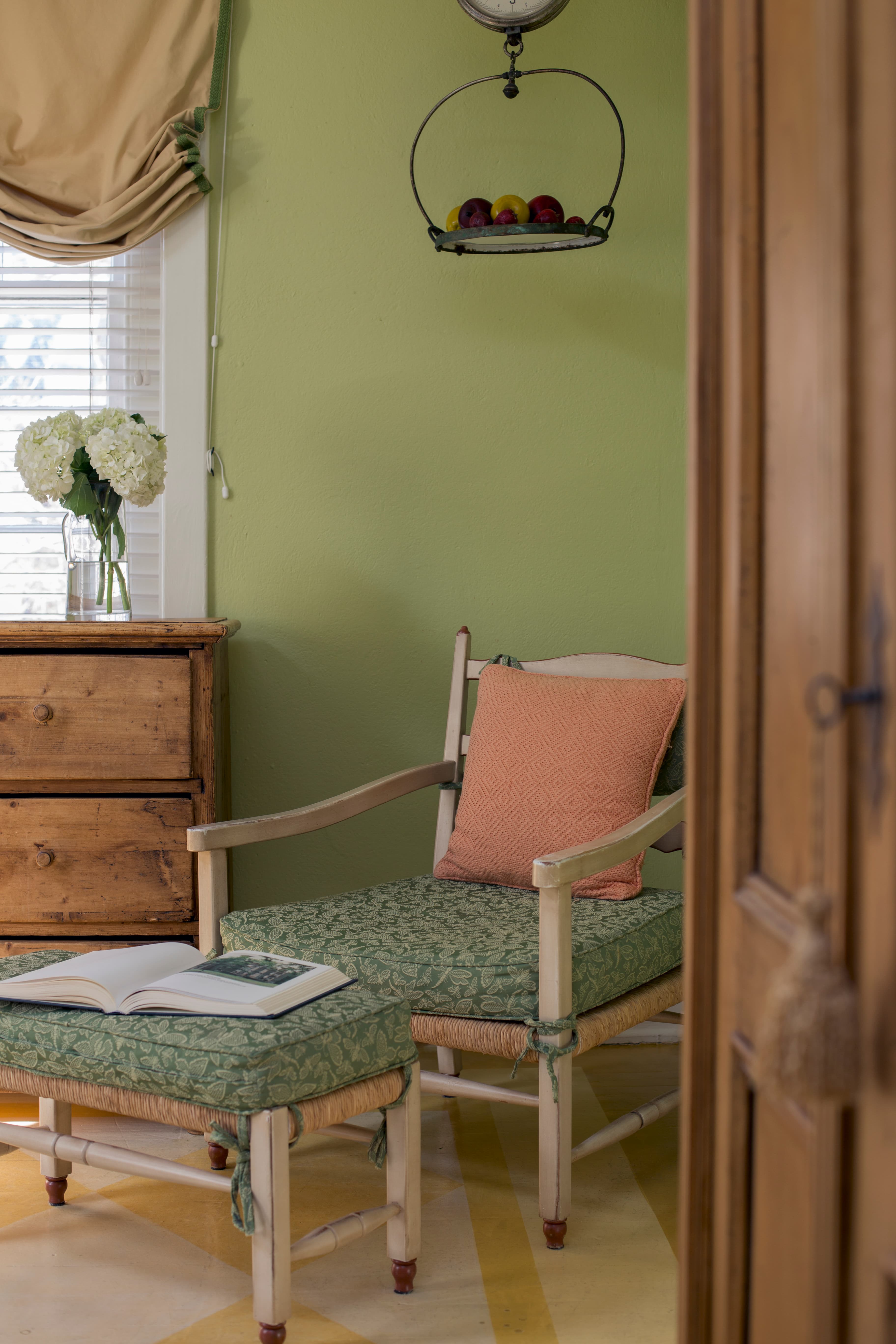 Wooden painted chair with cushions and matching footstool in corner of bedroom