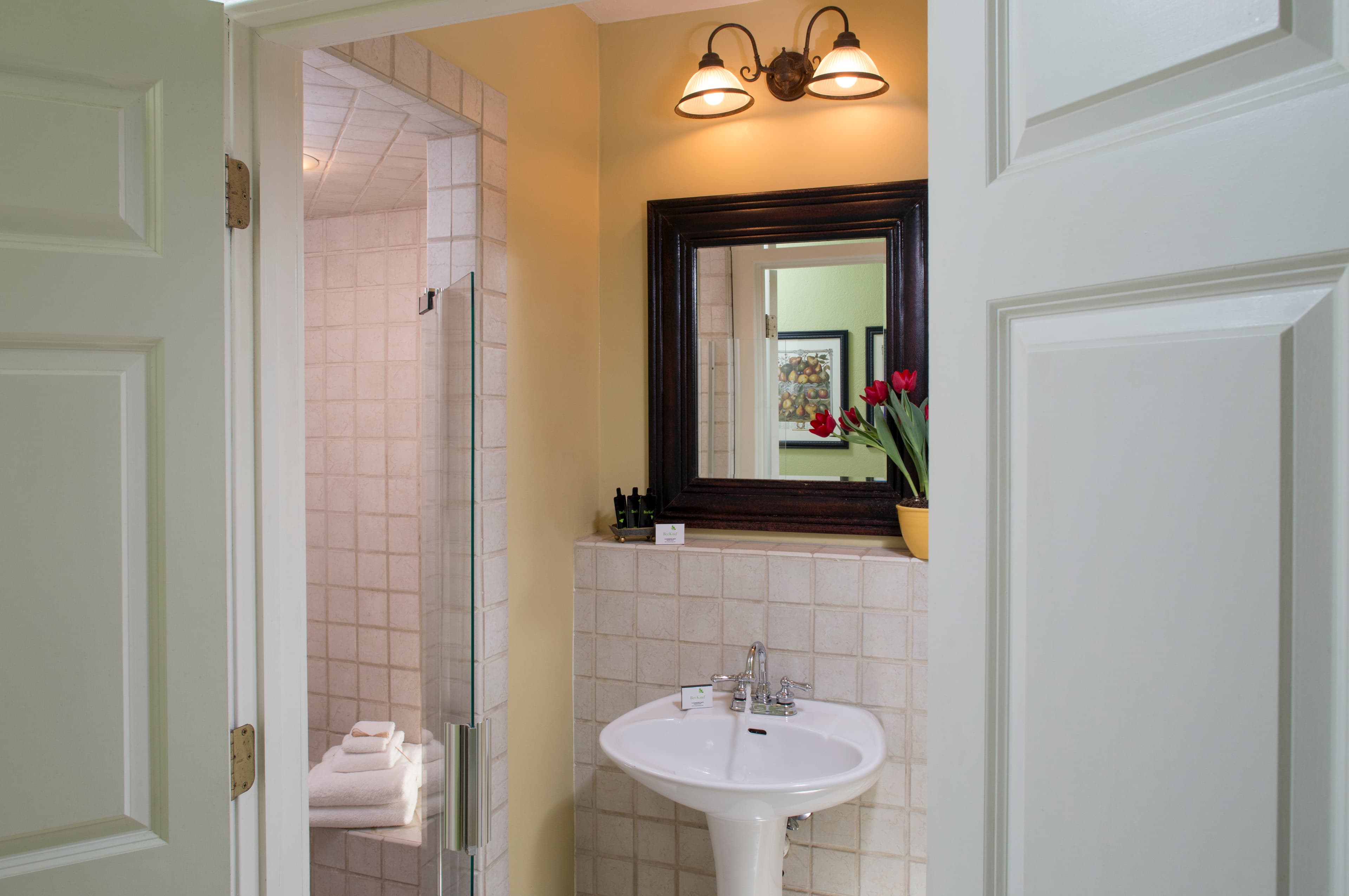 View of bathroom from doorway, white pedestal sink, framed mirror, tiled shower with glass doors