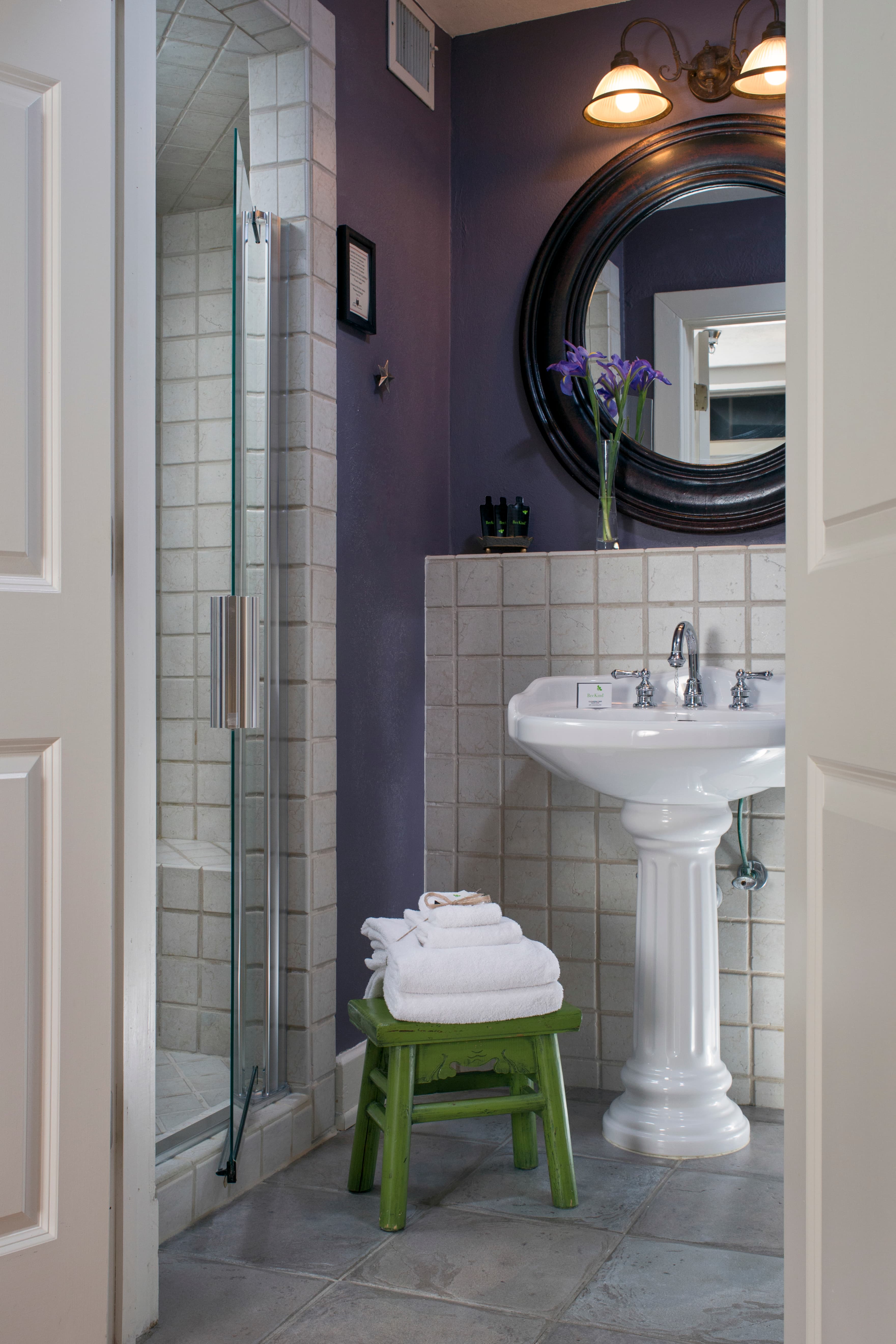 Bathroom with lavender walls, white pedestal sink, framed mirror, and tiled shower with glass doors